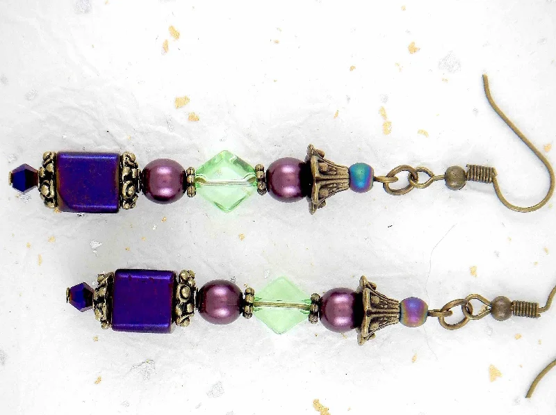 Long layered earrings with metallic violet cubes, plum balls, green lozenges, violet crystals, brass caps, brass hooks